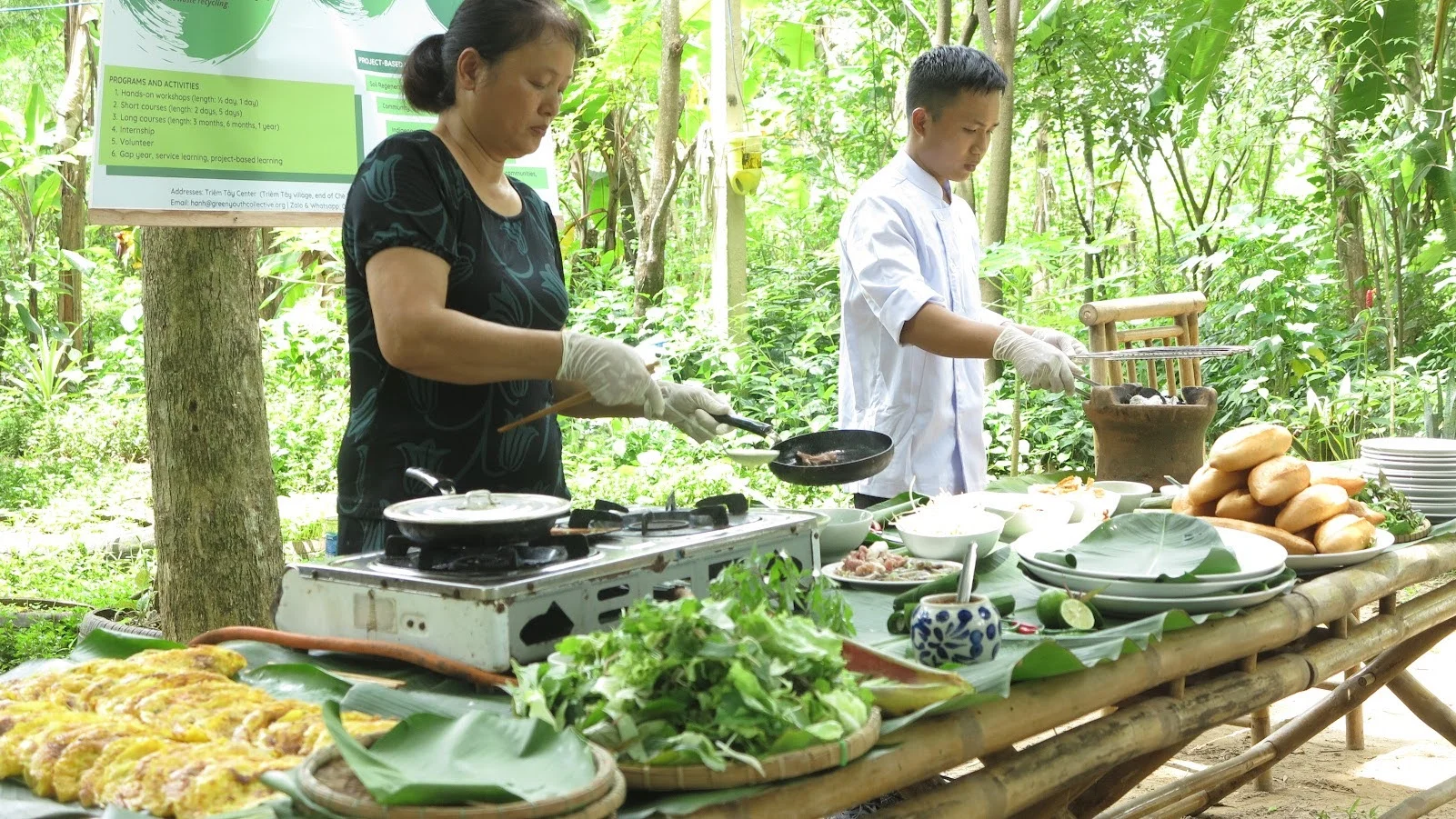 A traveler laughing while preparing spring rolls under the guidance of a local host during a private cooking class Hoi An.