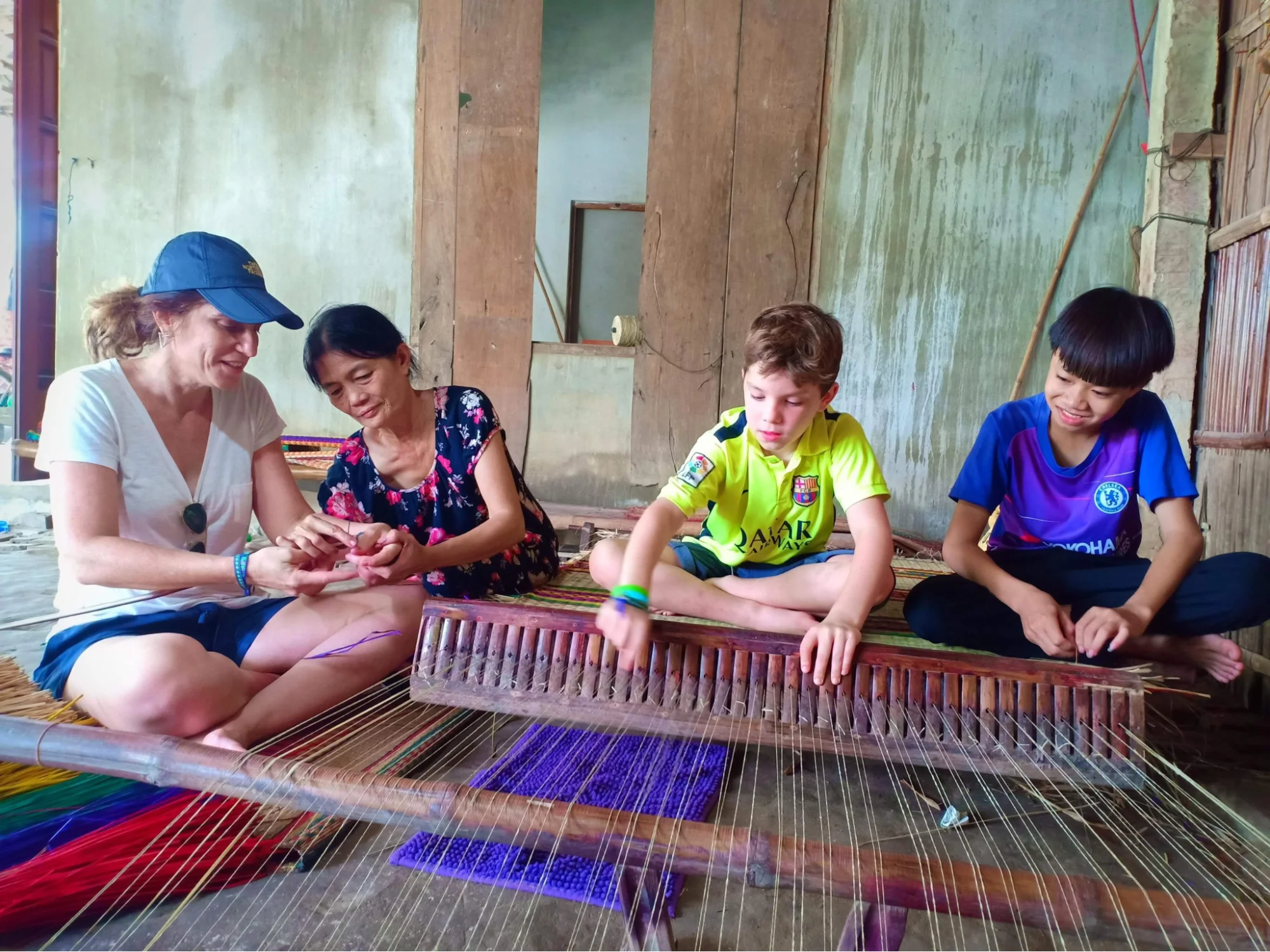 A traveler laughing with a local mat weaver in a village home on Cam Kim Island.