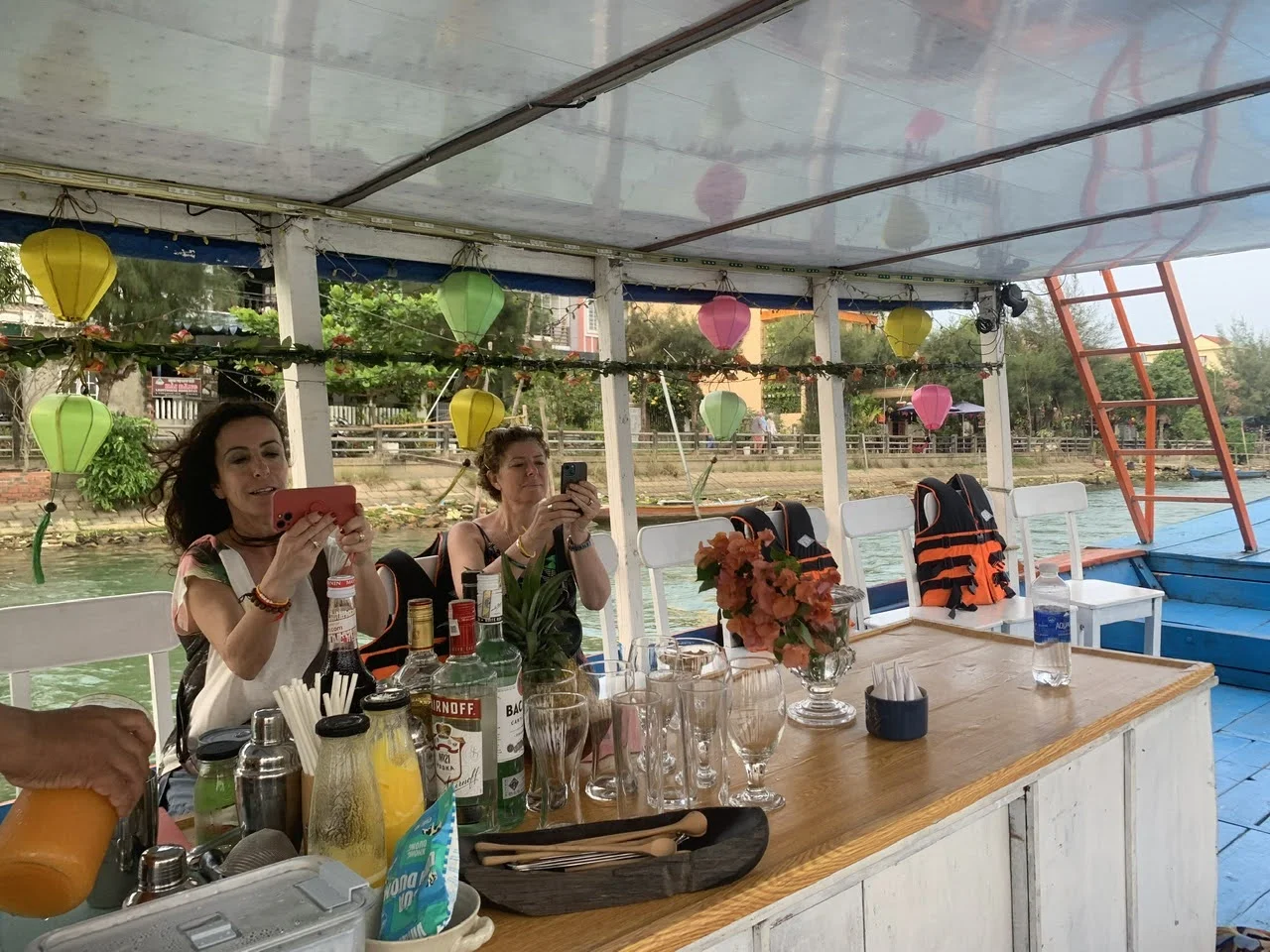A couple enjoy refreshing drinks on the deck of a boat while watching the sunset over the river on a Hoi An sunset river cruise.