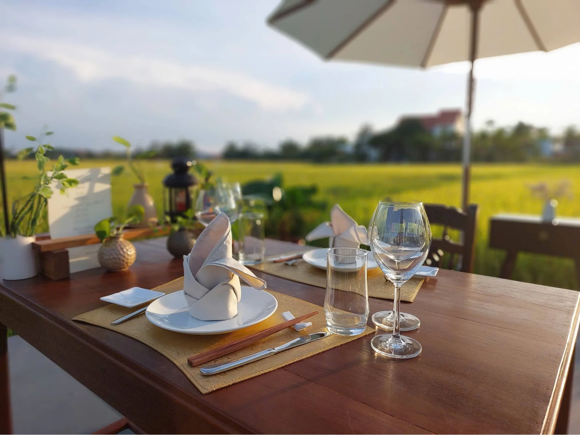 A beautifully set candlelit dinner table on a wooden platform in the middle of a rice paddy at sunset during a Hoi An private tour.