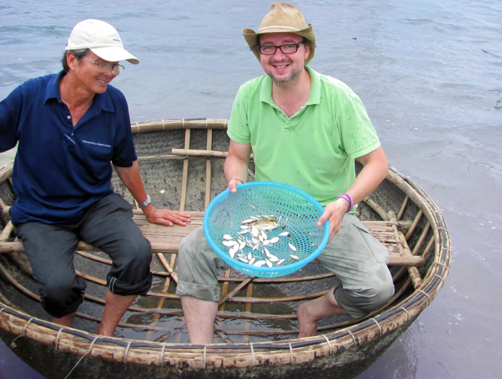 A happy tourist shows his fresh catch in a basket boat with a friendly local guide on an authentic Hoi An fishing tour.