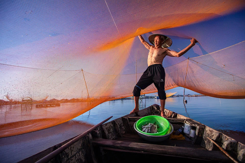 Local fisherman casting a large net during a Hoi An fishing tour on the Thu Bon River.