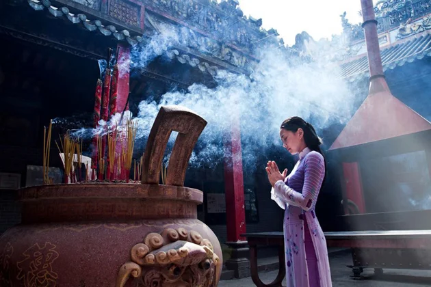 A woman praying before a large incense burner with smoke rising at the Cantonese Assembly Hall Quan Cong Temple.