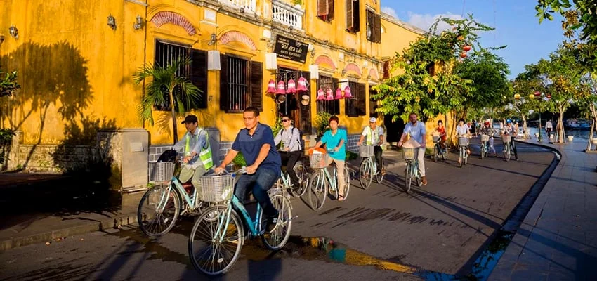 tourists cycling past historic yellow buildings on their way to enjoy authentic hoi an chicken rice