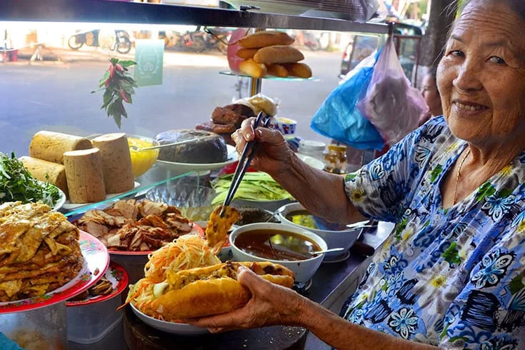 an elderly woman preparing banh mi at a famous street food stall near the Cantonese Assembly Hall