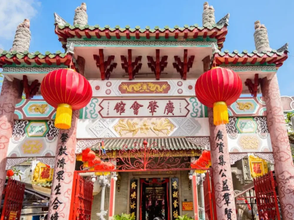 the vibrant and ornate front gate of the Cantonese Assembly Hall in Hoi An, adorned with red lanterns and traditional Chinese characters.