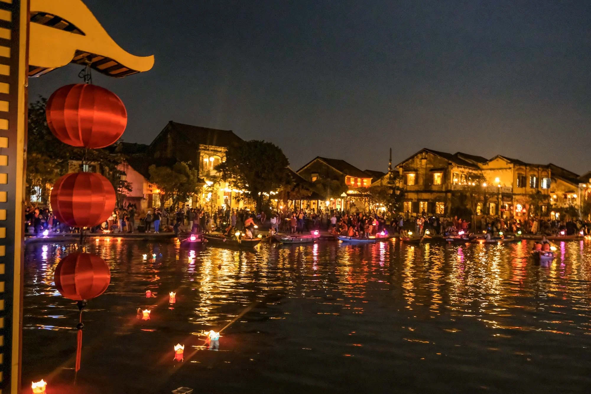 visitors enjoying Hoi An Lantern Festival boat rides on the Hoai River, surrounded by glowing lanterns and ancient town lights.