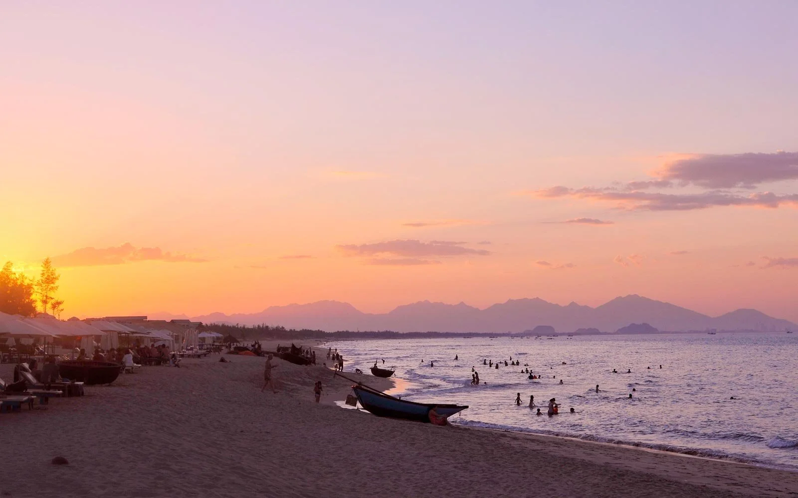 people swimming and relaxing on the sand under a colorful An Bang Beach sunset.