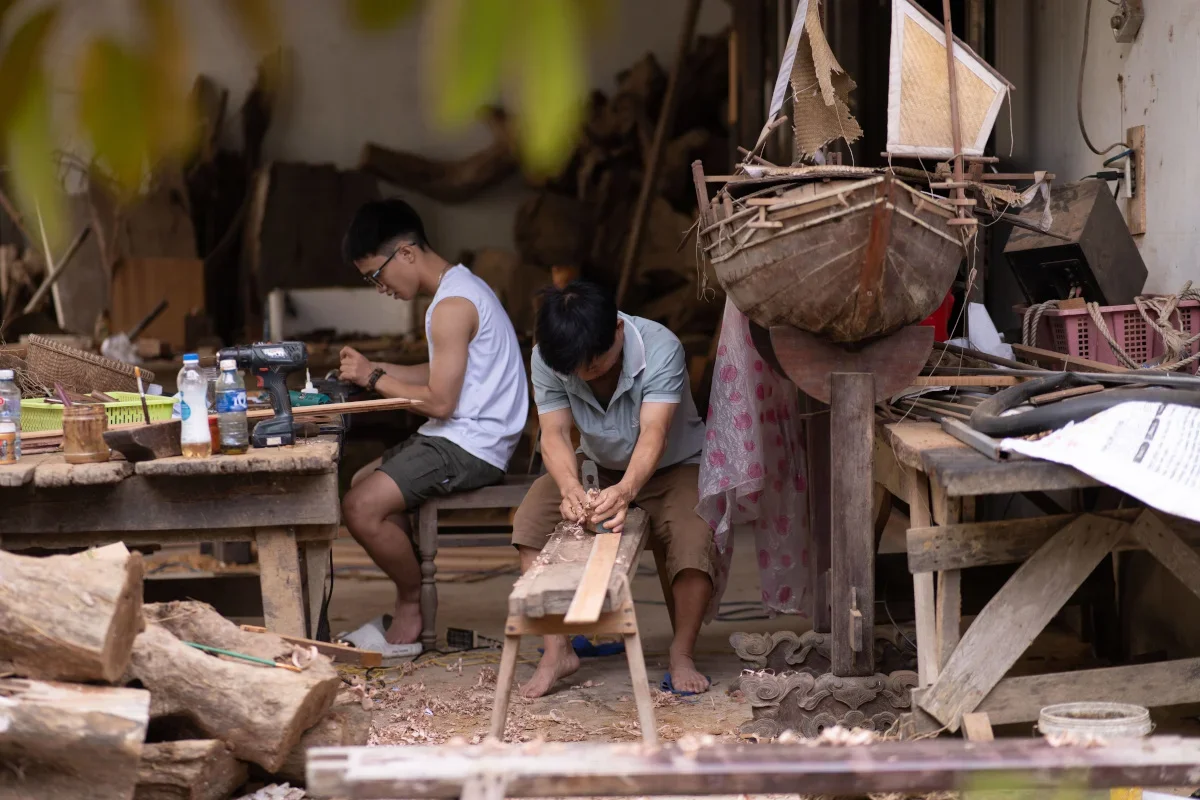 two artisans working on wooden pieces in a rustic workshop at Kim Bong Carpentry Village Hoi An