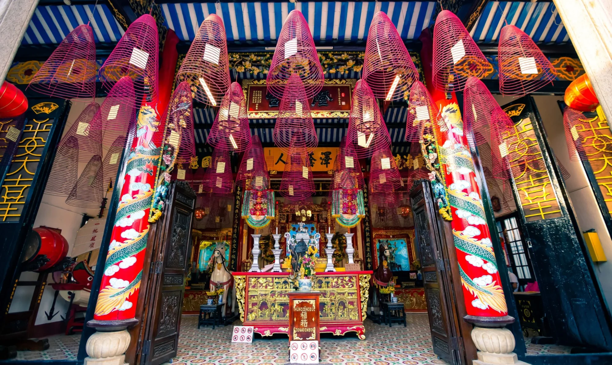 ornate interior of the Cantonese Assembly Hall Quan Cong Temple, featuring numerous spiral incense coils and a richly decorated altar.