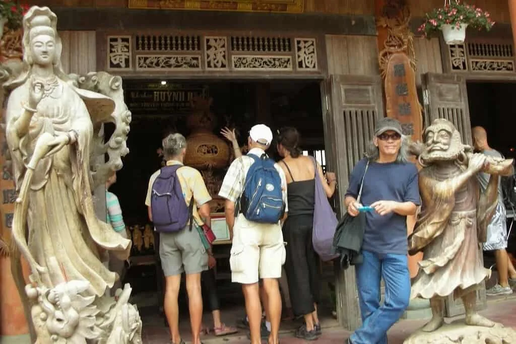 tourists admire large carved wooden statues and intricate entrance details at a workshop in Kim Bong Carpentry Village Hoi An