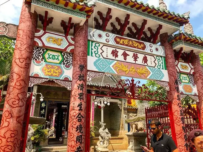 The vibrant, ornate entrance gate of the Cantonese Assembly Hall Hoi An, featuring traditional Chinese architecture and a visitor.