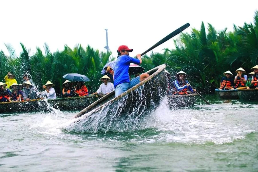 A person spinning a basket boat, making a big splash, while tourists watch from other boats, one of the exciting things to do in Hoi An.