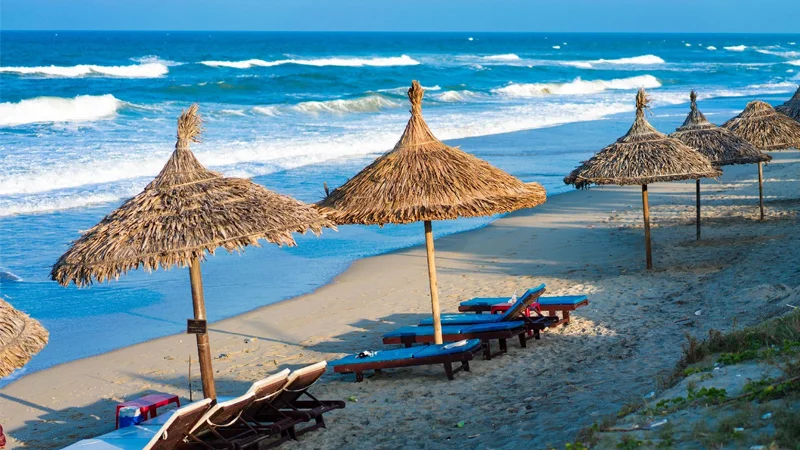 Relaxing straw umbrellas and lounge chairs on the white sands of An Bang Beach in Hoi An.