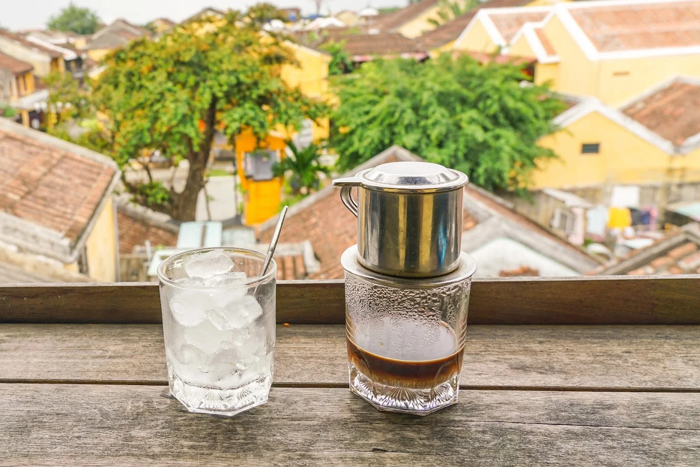 A traditional Vietnamese coffee with a phin filter and a glass of ice, overlooking the picturesque Hoi An Ancient Town, a relaxing experience among the things to do in Hoi An Ancient Town.
