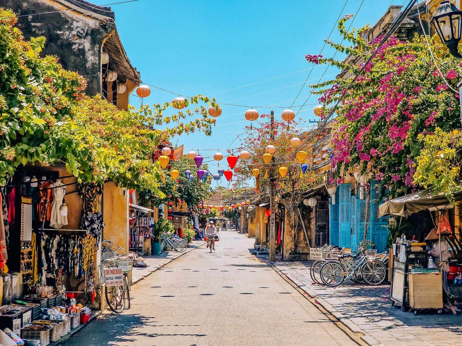 A person cycling down a street lined with yellow buildings and colorful lanterns, one of the top things to do in Hoi An.