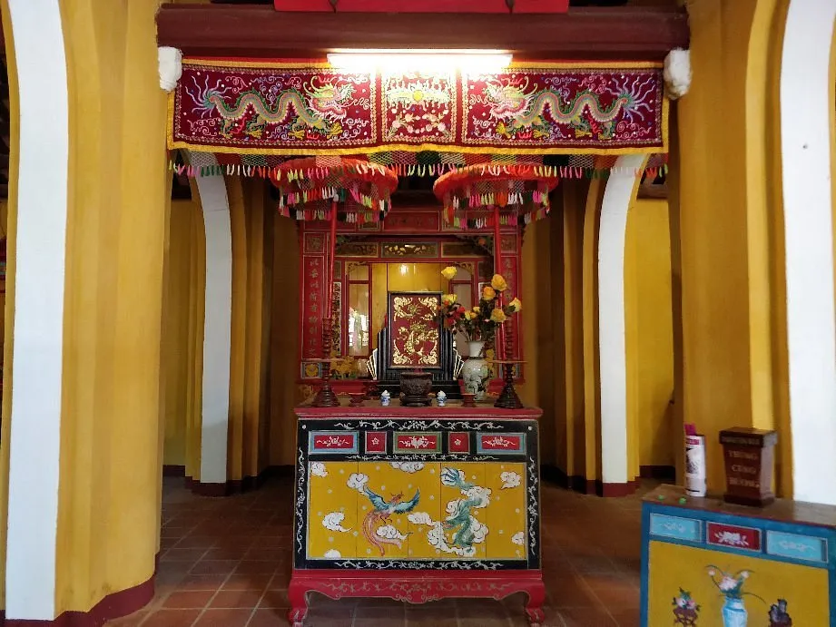 Ornate wooden altar and donation box inside Cam Pho Communal House.