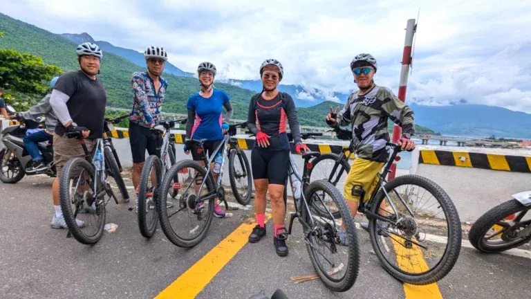 Group posing with a mountain bike rental Hoi An on a scenic coastal road.