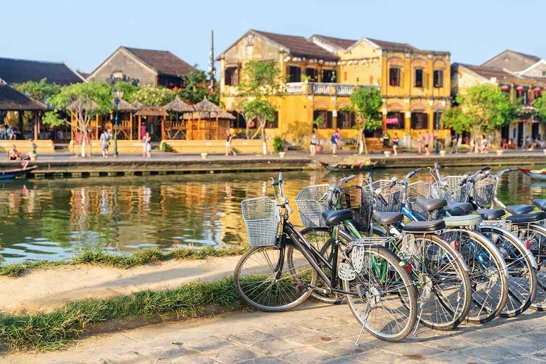 Bicycles parked by the river near ancient yellow buildings on a Hoi An cycling route.