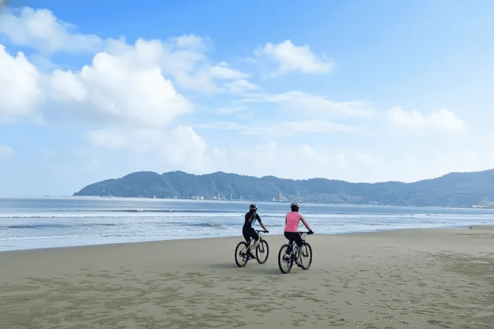 Two cyclists riding on a sandy beach along a coastal Hoi An cycling route.