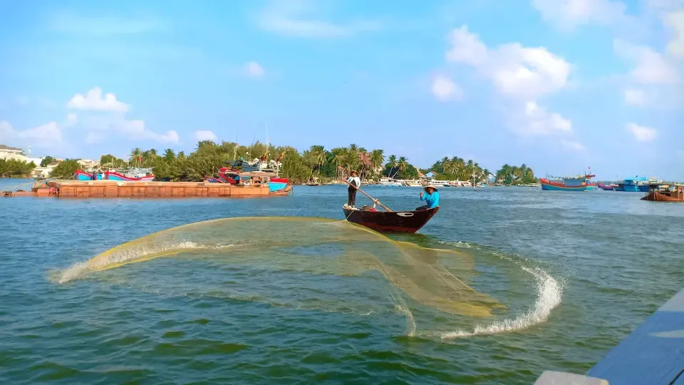 Fishermen casting a large net from a wooden boat near a Hoi An fishing village.