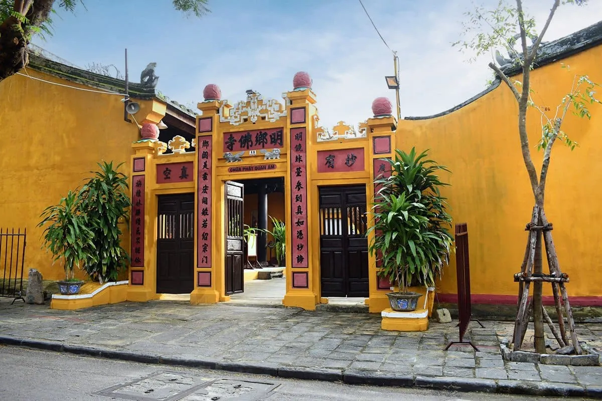 Yellow entrance gate to Quan Am Pagoda featuring open wooden doors and stone pavement at quan am pagoda hoi an