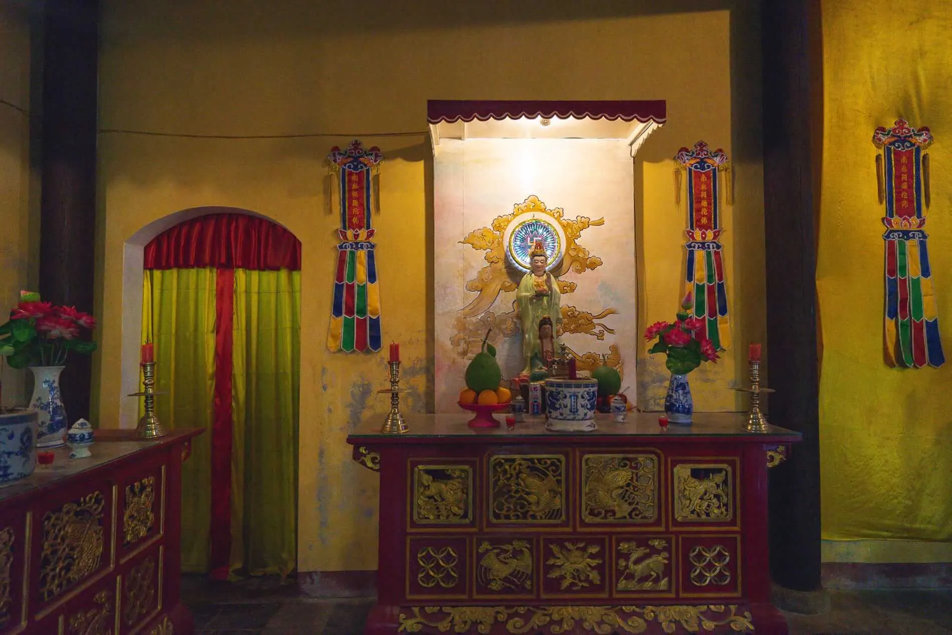 Red wooden altar at Quan Am Pagoda Hoi An with a statue and fresh fruit.