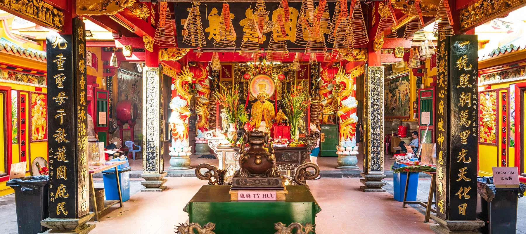 Ornate temple interior with red pillars, hanging incense coils, and a central altar at quan am pagoda hoi an