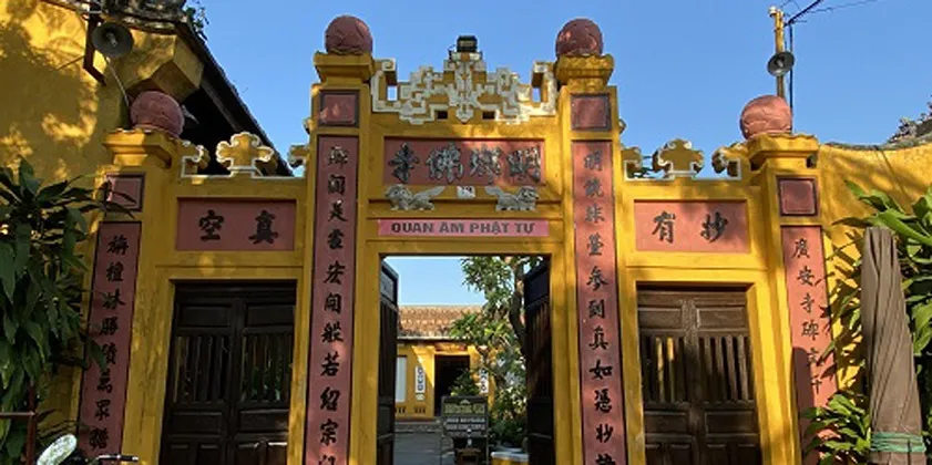 Yellow three-arched temple gate with open center doors and Chinese inscriptions at quan am pagoda hoi an