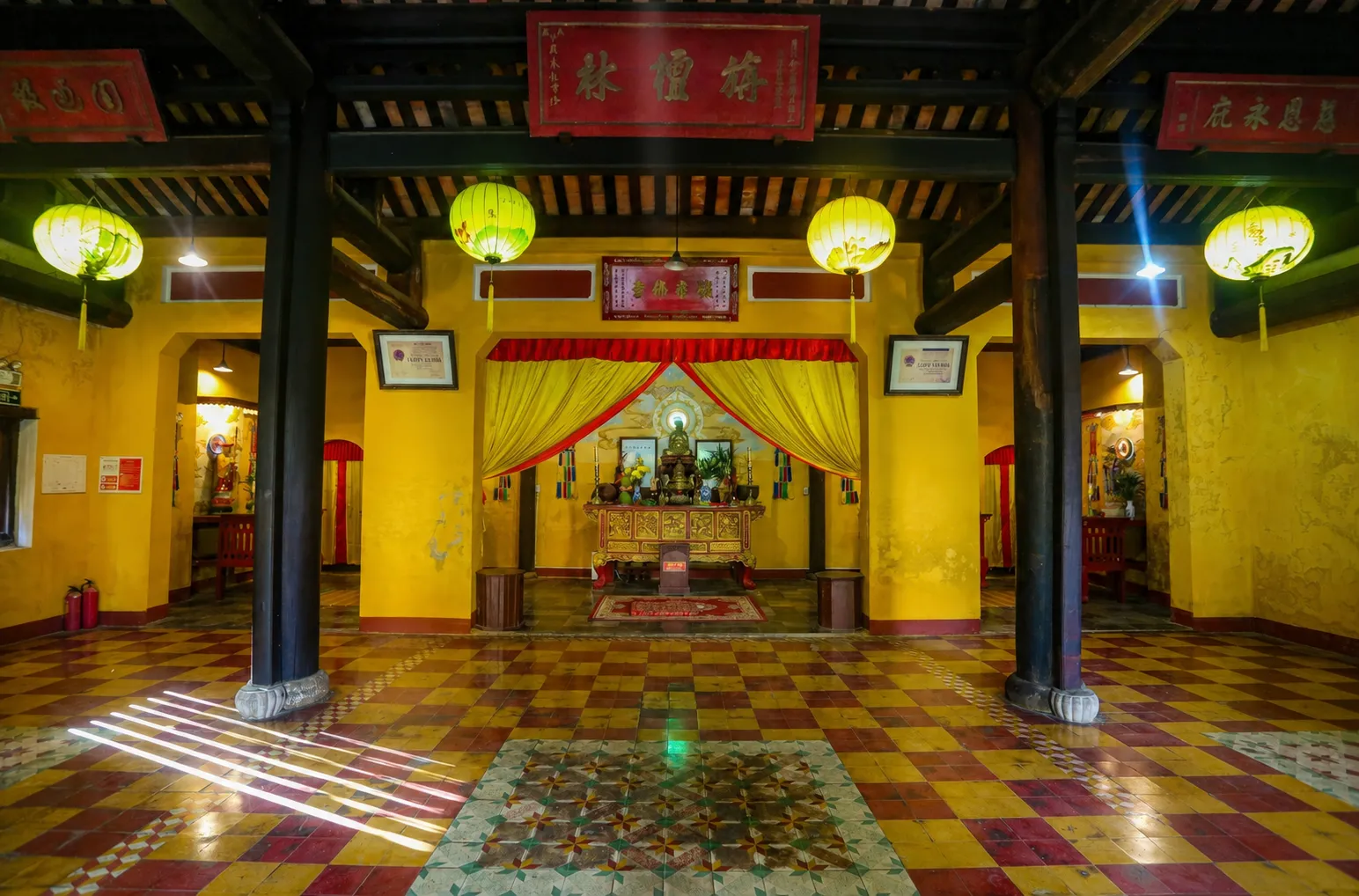 Temple interior with dark wooden pillars, patterned floor tiles, and a central altar at quan am pagoda hoi an