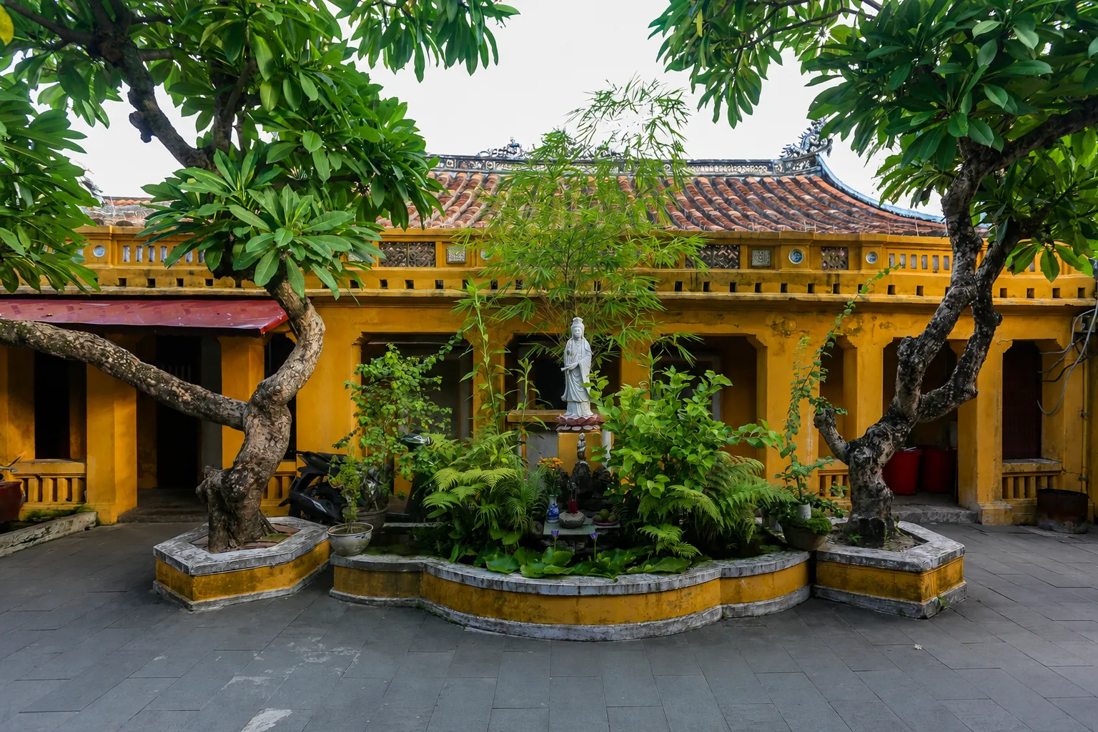 White Quan Am statue surrounded by greenery in a yellow temple courtyard at quan am pagoda hoi an