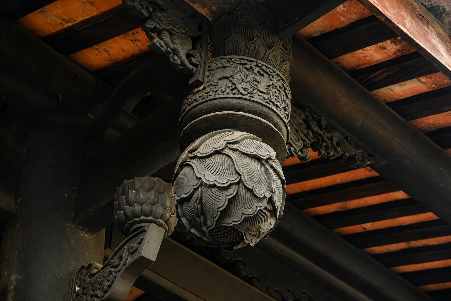 Close-up of an intricately carved wooden lotus bracket under a terracotta tiled roof at quan am pagoda hoi an