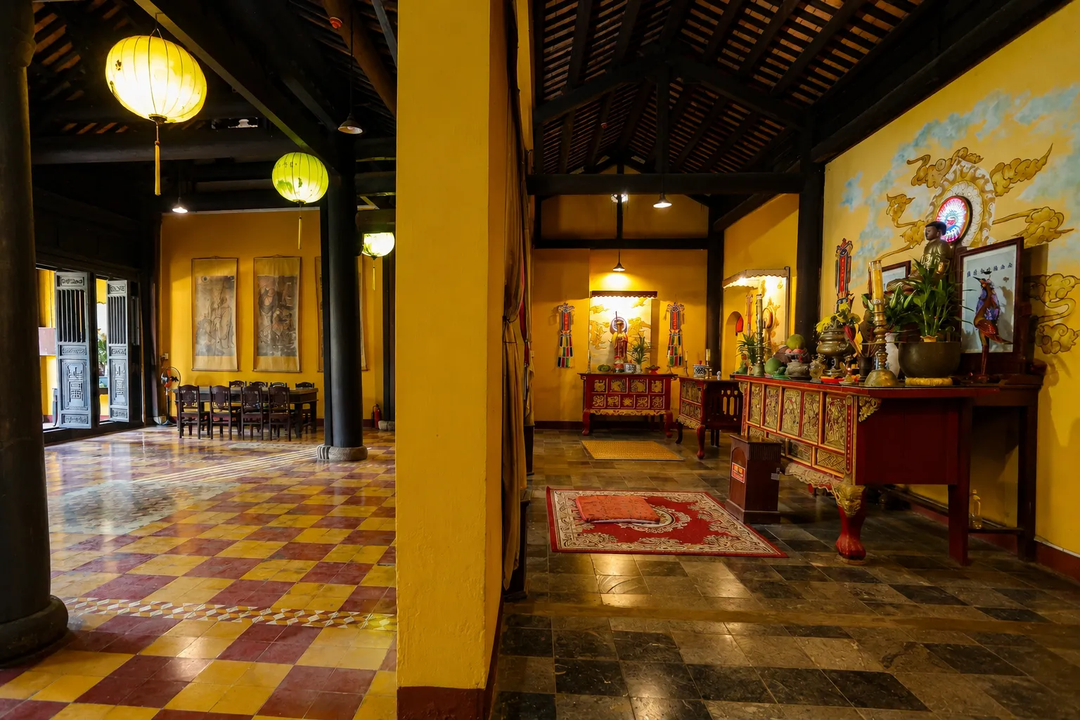 Spacious yellow temple interior featuring dark wooden pillars, lanterns, and a red altar at quan am pagoda hoi an