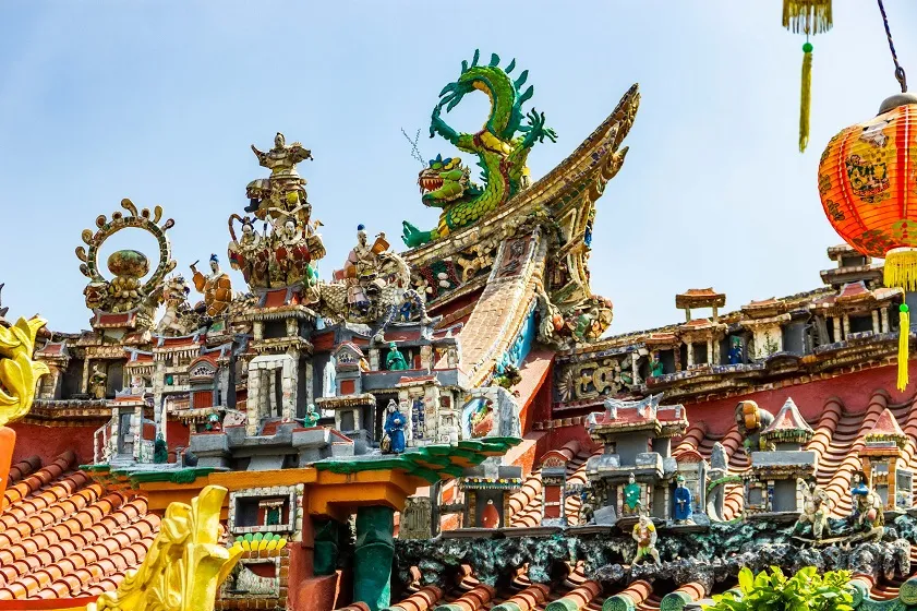 Ornate terracotta temple roof adorned with colorful ceramic mosaics and a green dragon at quan am pagoda hoi an