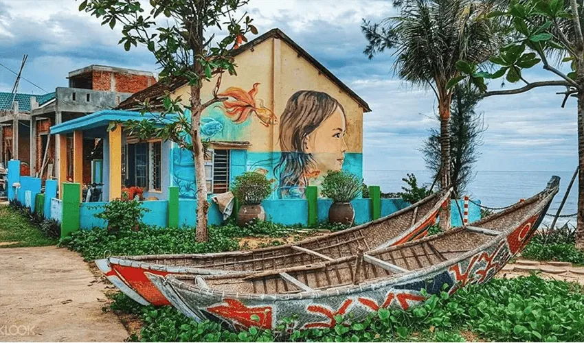 Painted boats near a vibrant house mural in Tam Thanh Mural Village.