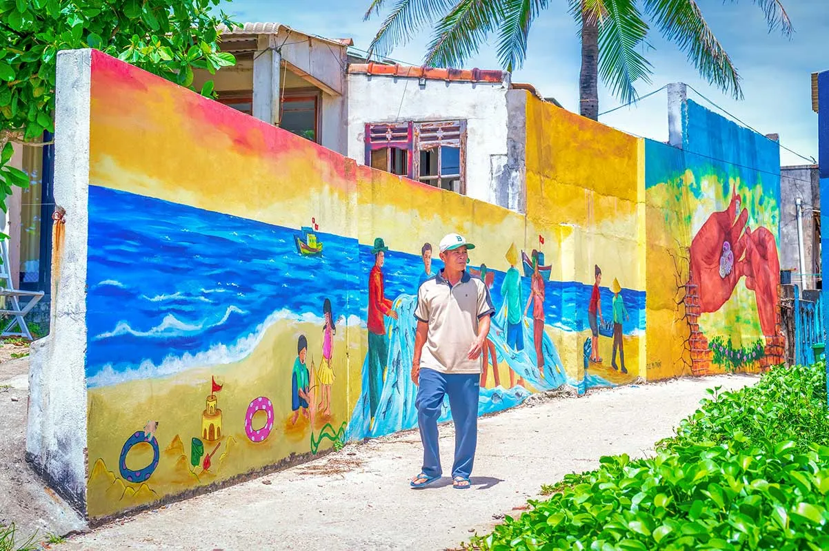 Local man walking past a bright beach mural in Tam Thanh Mural Village.