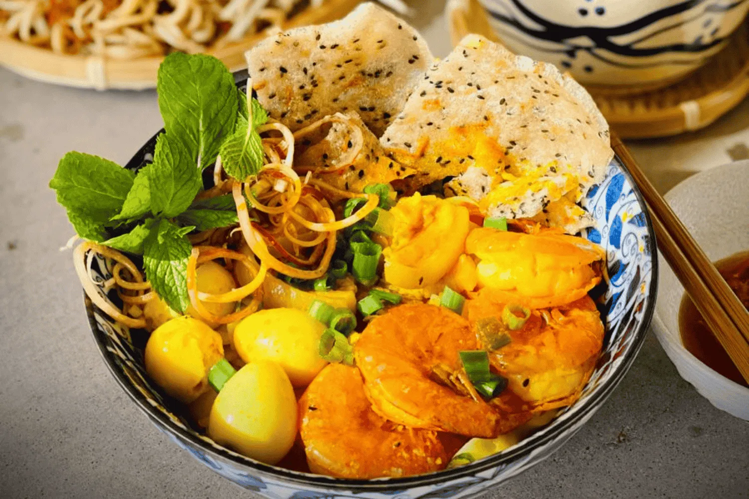 A bowl of traditional Mi Quang with shrimp, pork, herbs, and crispy rice crackers
