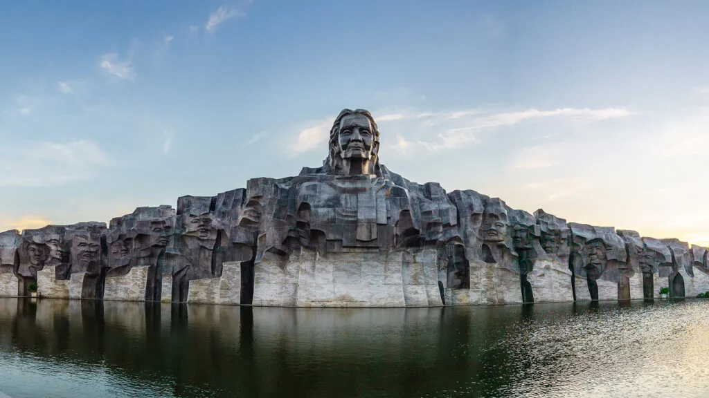 Large stone face monument reflecting in water near tam thanh mural village.