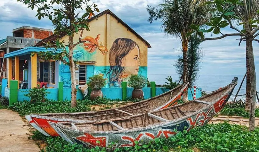 Painted traditional boats sit outside a vibrant home at tam thanh mural village.