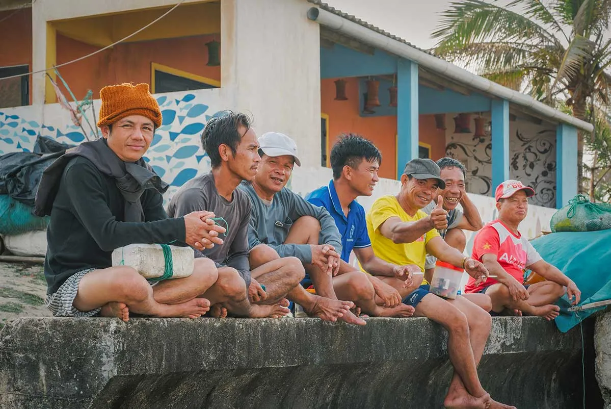Local men resting on a concrete ledge in Tam Thanh Mural Village.