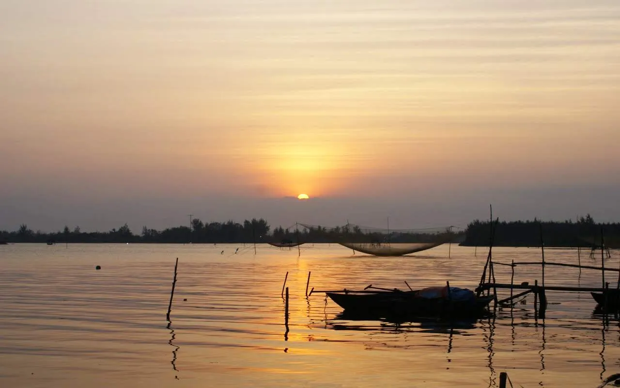 Traditional fishing nets and a small boat at sunset on the Thu Bon River.