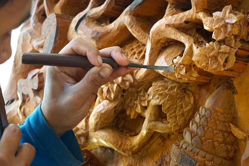 Hands carving intricate wood details with a chisel near the Thu Bon River Hoi An.